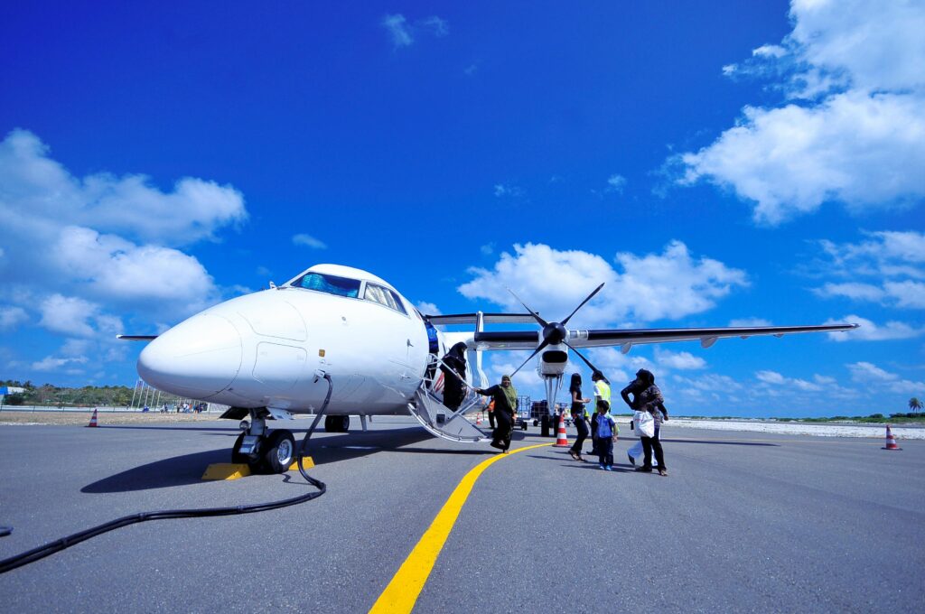 Photo by Asad Photo Maldives. Passengers disembark a small jet. Behind the jet, the sky is bright blue.